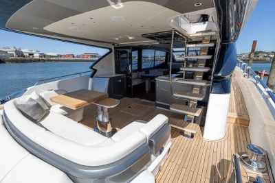 Luxurious 2023 Princess S72 yacht deck with seating, table, and staircase, docked by the water.