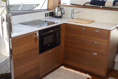 Modern kitchen in 2024 Princess F50 yacht with stove, microwave, and wooden cabinetry.