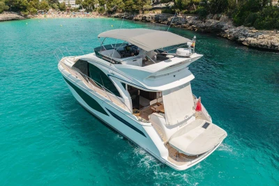 Luxurious 2024 Princess F50 yacht cruising in clear turquoise waters near a scenic coastline.