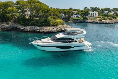 Luxurious 2024 Princess F50 yacht cruising in clear turquoise waters near a rocky coastline.