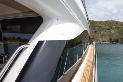 Sleek 2025 Princess F65 yacht with wooden deck, cruising near rocky shoreline.