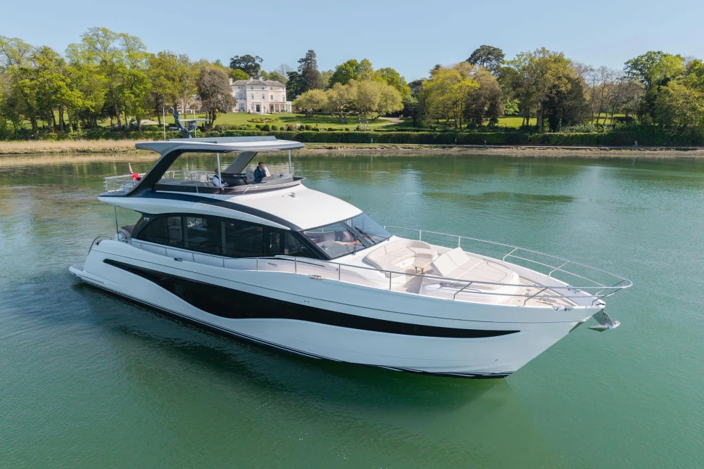 Luxurious 2026 Princess Y72 yacht cruising on serene waters near a lush, green shoreline.