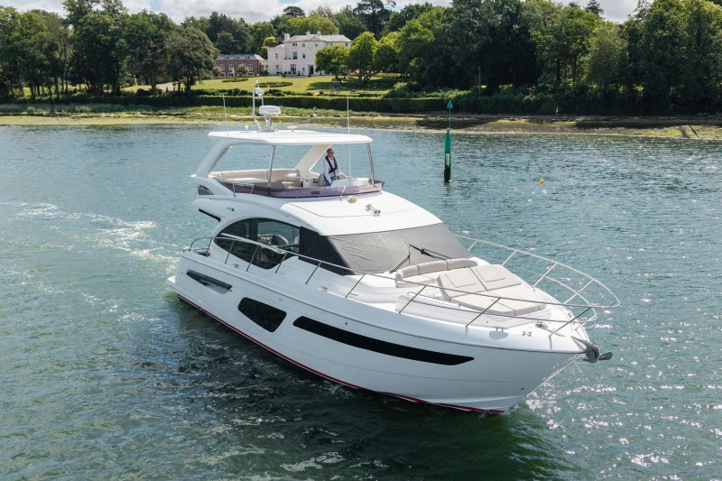Luxurious 2020 Princess F55 yacht cruising on a serene waterway near a lush shoreline.