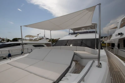 Sun deck of a luxury yacht with comfortable loungers and sunshade, docked at a harbor.