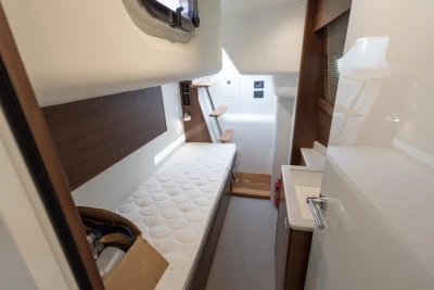 Interior of a modern yacht with a single bed, wood paneling, and a small sink.